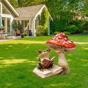 Garden statue featuring a green frog reading on a book under a red spotted mushroom