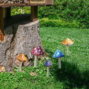 Five colorful plastic mushroom garden stakes arranged on grass near a wooden stump