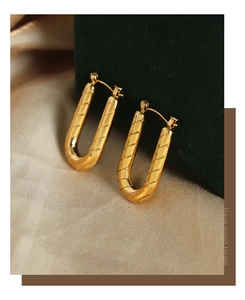 Macro shot of gold U-shaped earrings with diagonal twill texture on dark green velvet