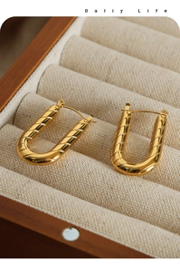 Macro view of gold-plated U-shaped hoop earrings with spiral twisted texture on linen