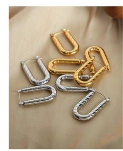 Macro detail of U-shaped gold and silver earrings with diagonal spiral texture on silk