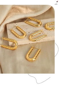 Close-up of gold-plated U-shaped earrings featuring a refined diagonal twill pattern texture
