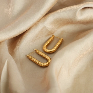 Chic U-shaped gold plated titanium earrings with diagonal texture on satin background