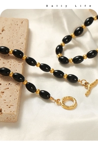 Detail of black oval beads and textured gold toggle clasp on a handmade necklace