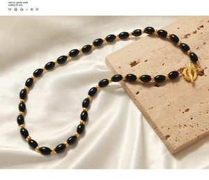 Close-up of black onyx beaded necklace with gold accents and decorative OT toggle clasp