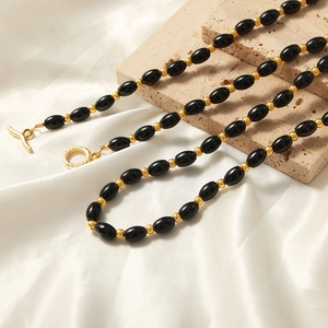 Natural black oval agate beaded necklace with gold toggle clasp on silk fabric