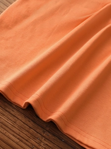 Detail of orange knitted tank top showing fine plain knit texture and double-stitched hem
