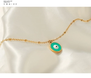 Gros plan d'un collier œil protecteur plaqué or avec émail vert sur de la soie blanche