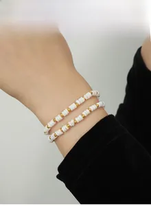 Close-up of white heishi shell beads and gold titanium beads layered on a woman's wrist