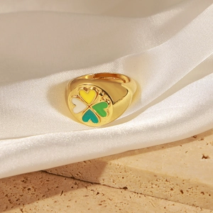 Gros plan d'une bague dorée avec trèfle en émail coloré sur fond de satin blanc pur