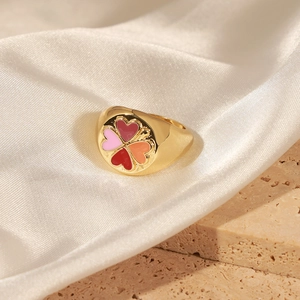 Détail d'une bague chevalière dorée avec trèfle en émail coloré sur soie blanche et pierre