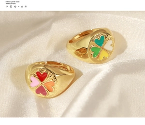 Détail de deux bagues dorées ajustables avec trèfles à cœurs colorés émaillés
