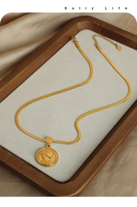 Detail of 18k gold plated portrait coin pendant with flat snake chain on silk background