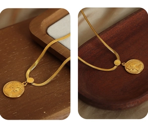 Detail of a vintage gold portrait coin pendant on a flat snake chain necklace