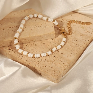 Minimalist white shell and gold steel bead bracelet on a warm stone and silk background