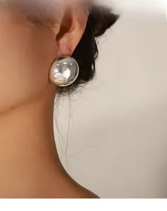 Close-up of oversized silver metallic dome stud earring with high-polish mirror finish