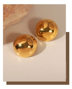 Close-up of polished gold sphere earrings with mirror finish on wooden background