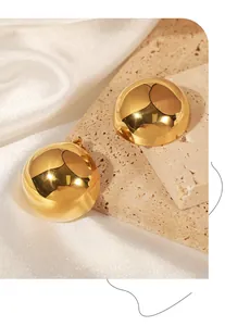 Macro shot of large hollow gold dome earrings on elegant stone and silk background