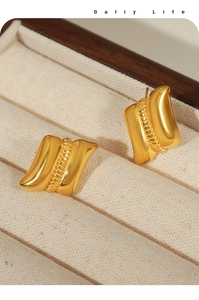 Macro detail of gold geometric wave earrings with central bead line in jewelry box
