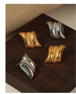 Macro detail of wave textured geometric gold and silver earrings on wooden stand