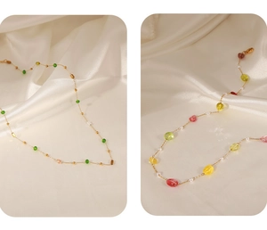 Détail du collier chaîne dorée avec perles colorées et nacrées sur un tissu en soie doux