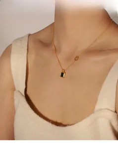 Close-up of gold-plated necklace with black rectangular pendant and small hollow heart detail