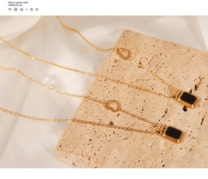 Detail of gold necklace with black rectangular pendant and heart link on silk fabric
