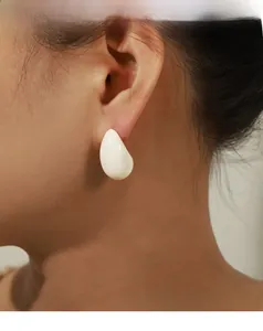 Close-up of white enamel teardrop stud earrings in 18k gold plating on a model
