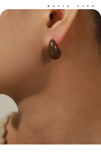 Close-up of deep brown teardrop earring with amber gloss finish on a model's ear