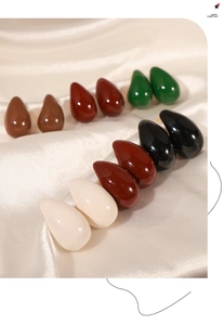 Close-up of teardrop enamel stud earrings in six colors on beige silk fabric