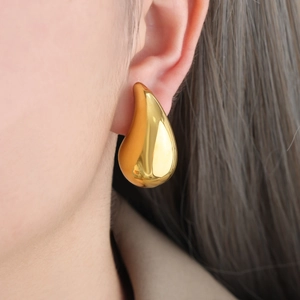 Detail of chunky gold teardrop earring with high-polish finish on a female model