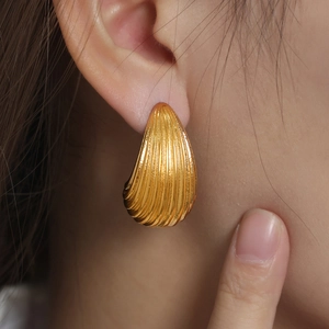 Macro detail of gold-plated drop earrings with vertical ribbed texture on earlobe