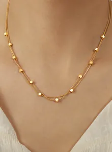 Gros plan sur un collier double rang en maille serpent dorée avec perles cubes