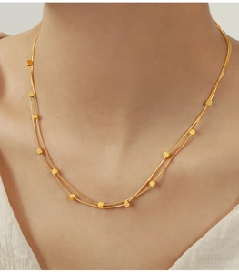 Gros plan d'un collier double épaisseur en acier titane doré avec des perles cubiques
