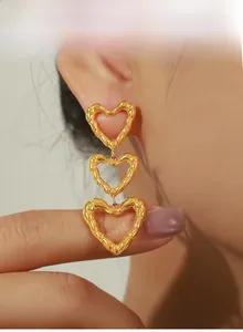 Macro shot of gold-plated triple heart drop earrings with bamboo texture on female model