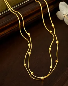 Détail de collier chaîne serpent dorée avec perles cubes sur plateau vintage