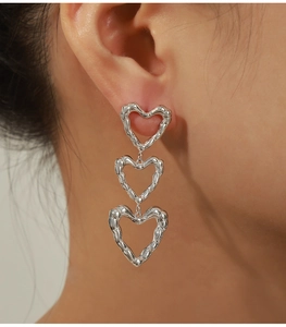 Close-up of three silver hollow heart drop earrings with liquid metal texture on a model