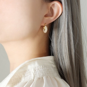 Boucles d'oreilles créoles torsadées dorées avec zircons portées par un mannequin