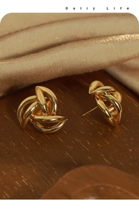 Close-up of twisted gold knot earrings on luxury wood and champagne satin surface