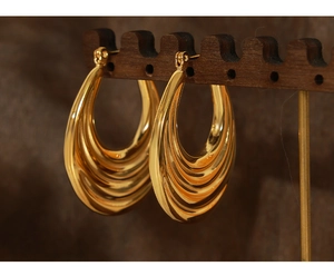 Macro shot of gold-plated titanium earrings with multi-layered wave texture on wood stand