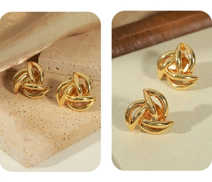 Detailed view of gold-plated geometric knot earrings on a beige travertine surface