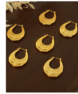 Detail of gold-plated croissant hoop earrings with elegant textured wave patterns on wood