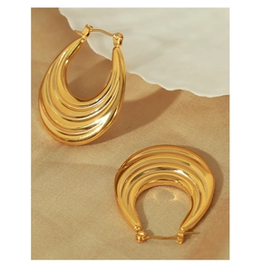Close-up of chunky gold hoop earrings with wavy texture on elegant fabric background