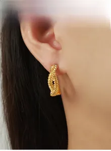 Close-up of golden twisted C-shaped hoop earring with textured rope design on model
