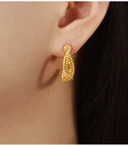Detail of gold spiral textured C-shaped earring on model showing irregular woven design