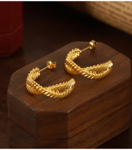 Detail of twisted rope gold C-shaped earrings resting on a vintage wooden jewelry box