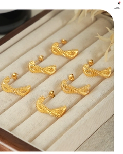 Detail of gold twisted cable hoop earrings arranged in a beige velvet jewelry display box