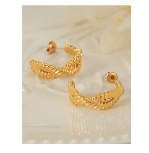 Detail of gold twisted rope C-shaped hoop earrings with intricate braided metal texture