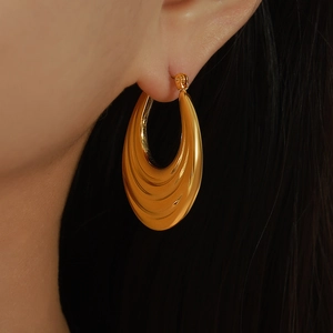 Polished gold-plated chunky crescent hoop earrings featuring textured drop design on model
