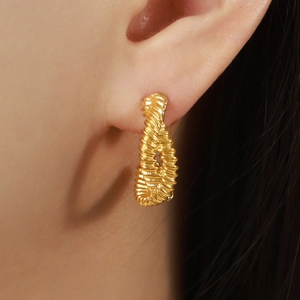 Chic twisted C-shaped gold hoop earring with spiral texture shown on model